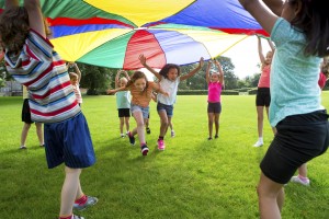 Kids lifting multi-colored parachute and running under it