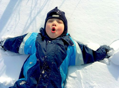 Toddler in snowsuit enjoying winter, making a snow angel. Omaha Dentistry